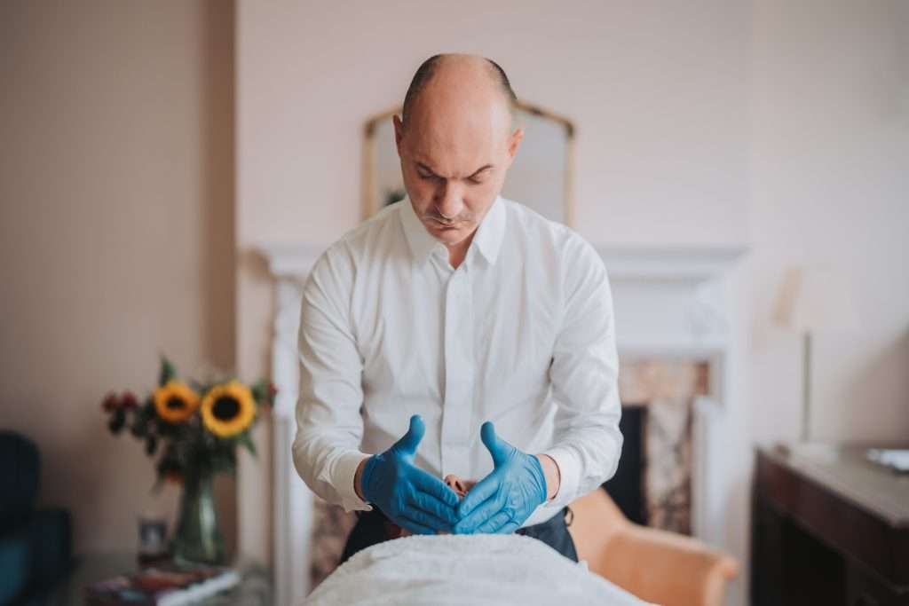 John Tsagaris conducting a facial acupuncture consultation in a London clinic room